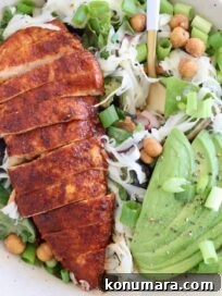 sliced buffalo chicken on top of a salad with sliced avocado