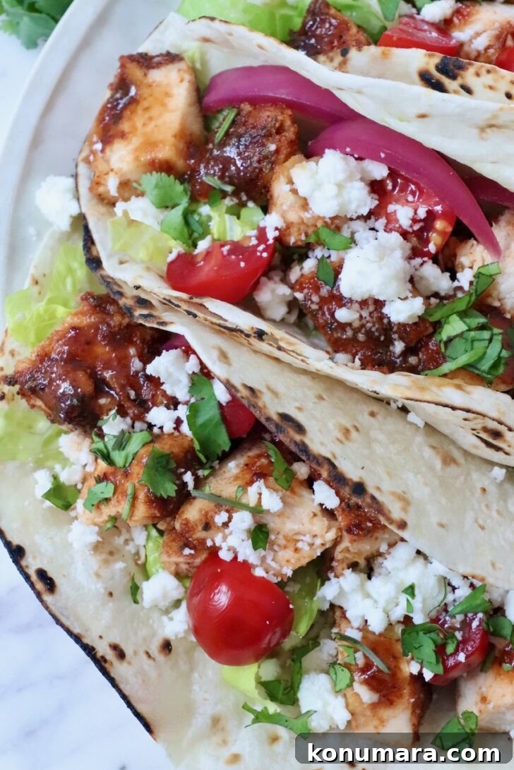 air fryer chicken tacos topped with diced tomatoes, pickled onions, cilantro, lettuce, and crumbled cheese on lightly charred tortillas.