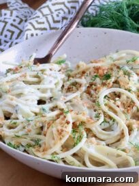 Creamy Dill Pickle Pasta Recipe 14 spaghetti in a creamy pickle sauce in a bowl with a fork, topped with toasted breadcrumbs