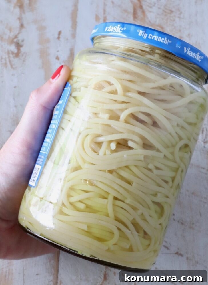 Creamy Dill Pickle Pasta Recipe 6 spaghetti noodles in a jar of pickle juice, with a hand holding the jar