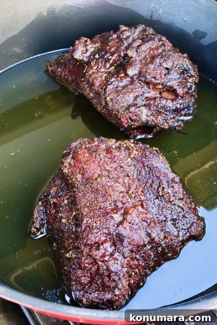 beef cheeks sitting in melted beef tallow in a cast iron skillet on a smoker