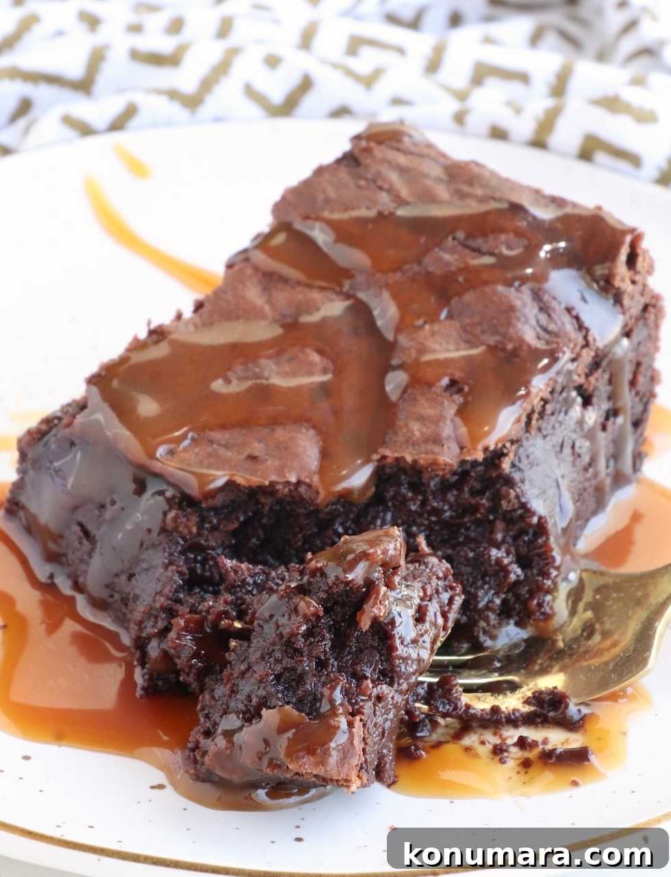fudgy brownie on a plate topped with caramel sauce with a bite cut out of it with a fork