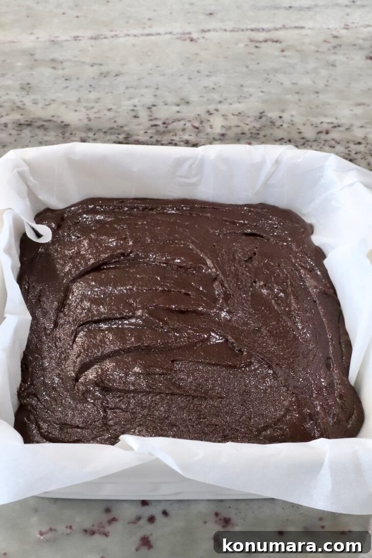 prepared brownie batter in a square baking dish lined with parchment paper