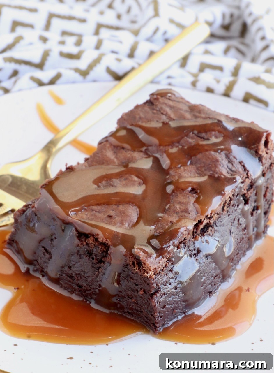 brownie on a plate covered in caramel sauce with a fork on the side