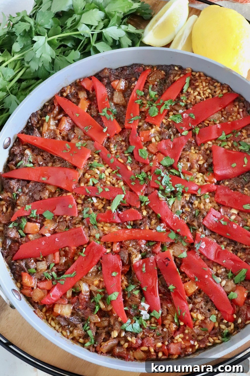 oxtail paella in skillet topped with sliced peppers with parsley and lemon wedges on the side