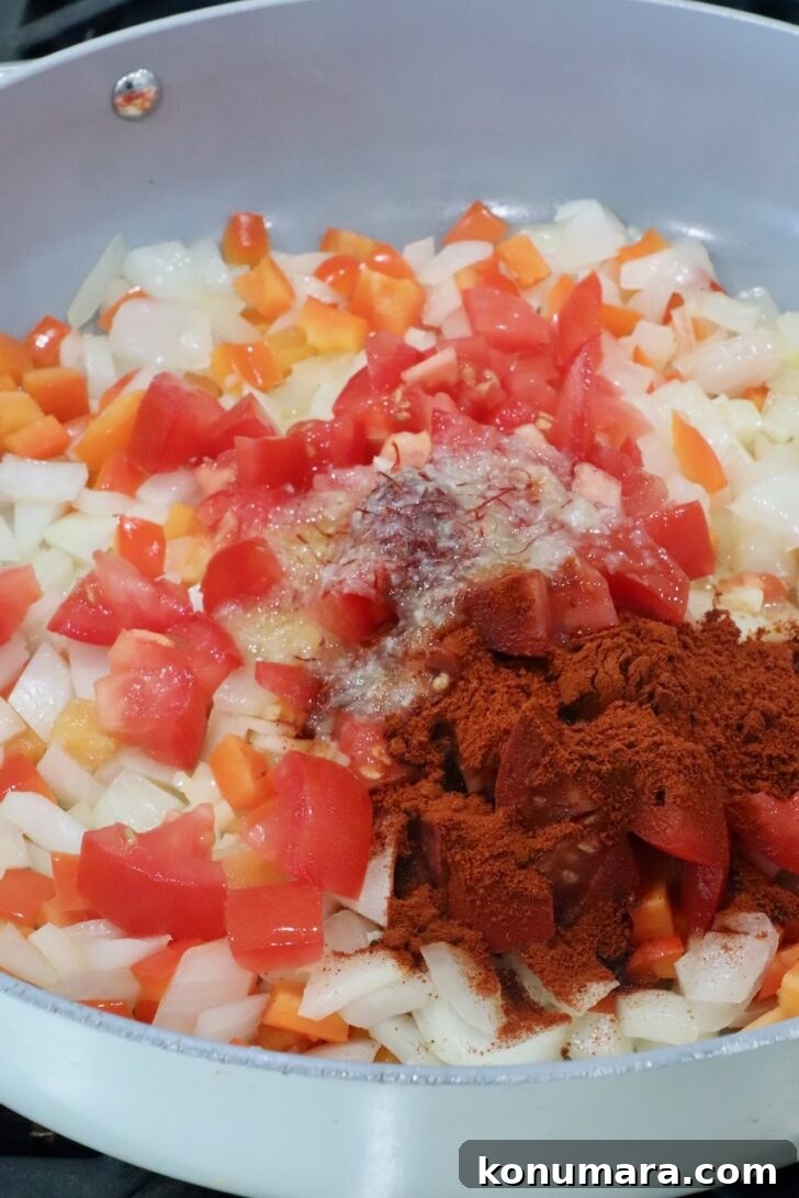 cooked diced onions, peppers and tomatoes covered in spices in a large skillet