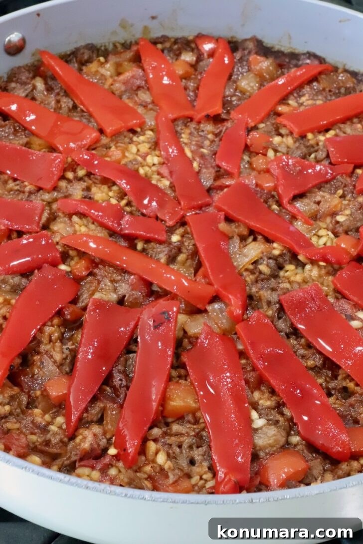 oxtail paella in a skillet topped with sliced piquillo peppers