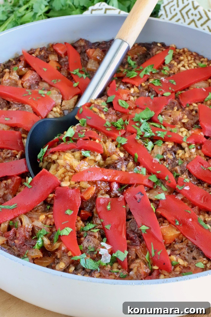 paella topped with sliced peppers in a large skillet with a serving spoon in the middle
