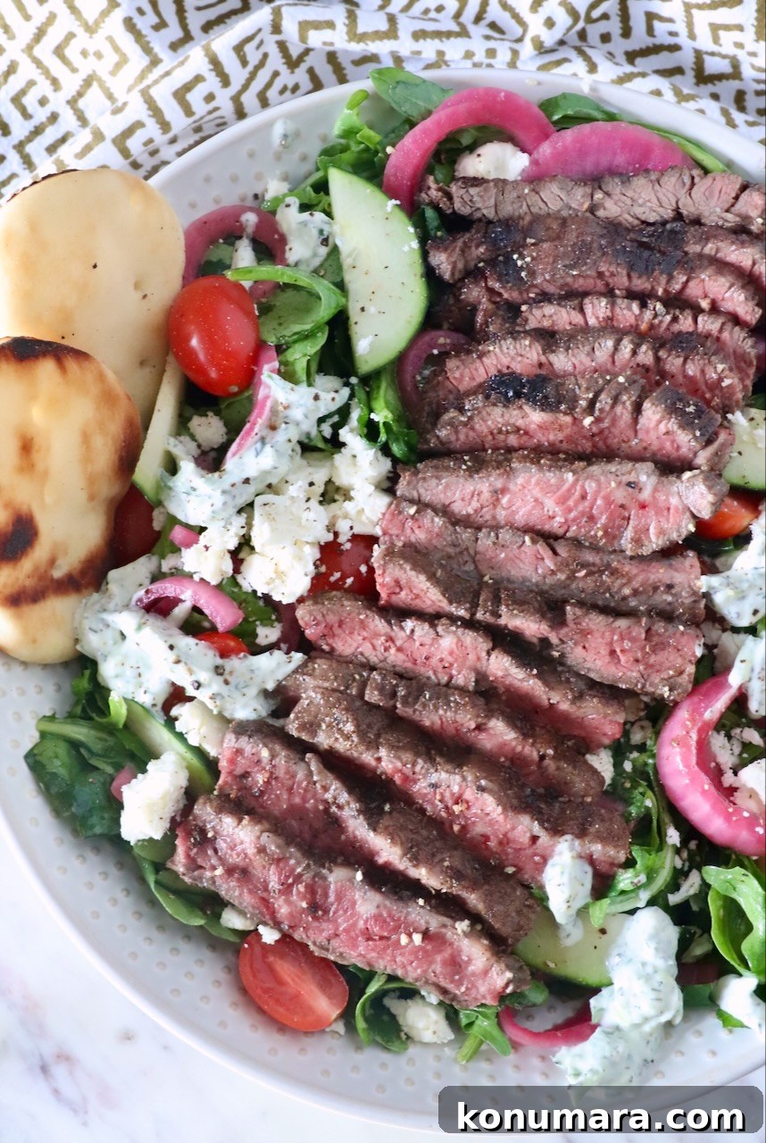 sliced grilled steak on top of a salad in a bowl with feta cheese, tomatoes and cucumbers