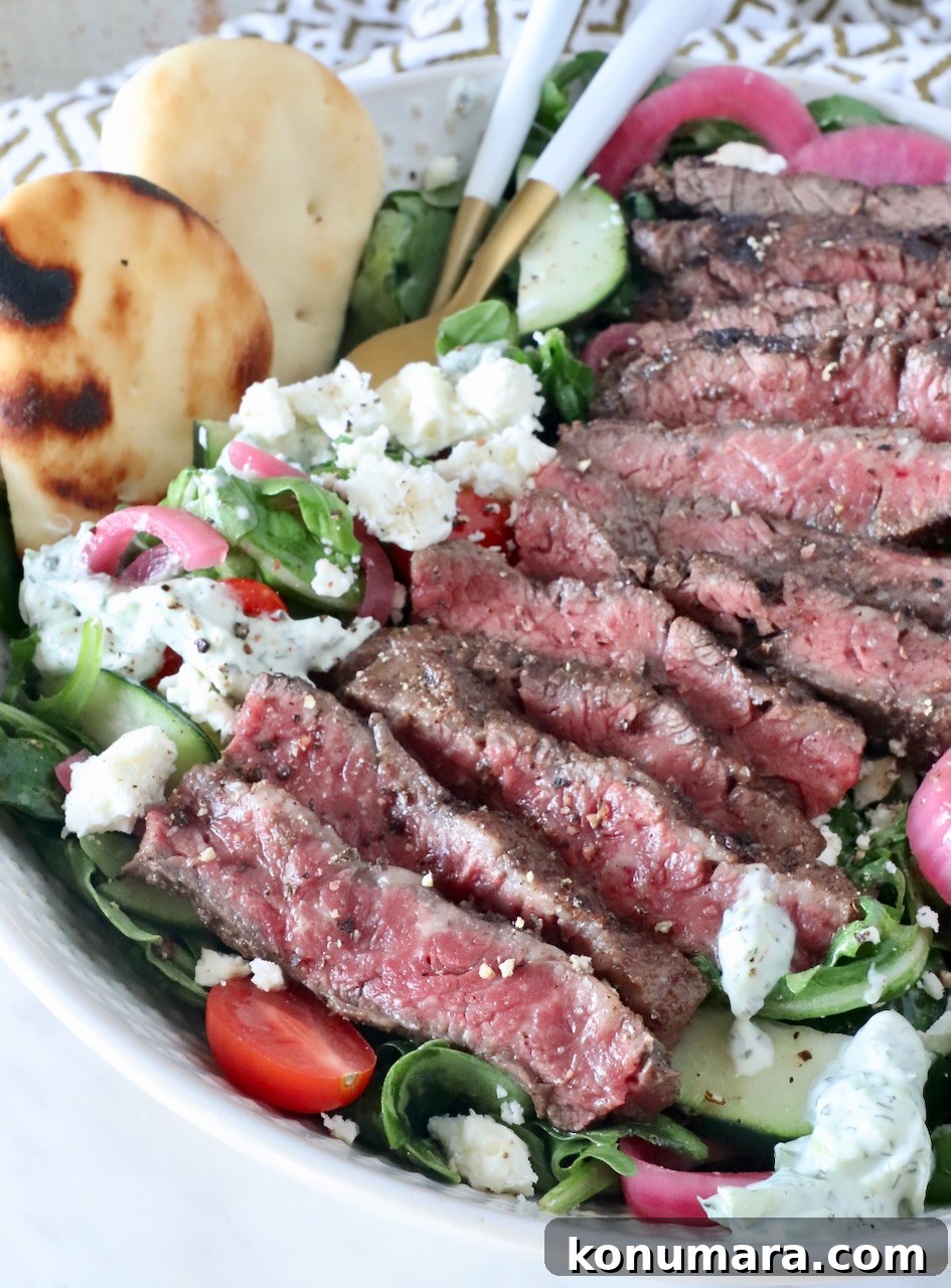 sliced grilled steak on a salad in a bowl with mini naan on the side and forks in the salad