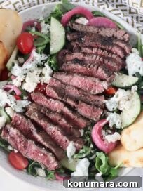 sliced shawarma grilled steak on top of a salad in a bowl with naan dippers, tomatoes, and feta cheese