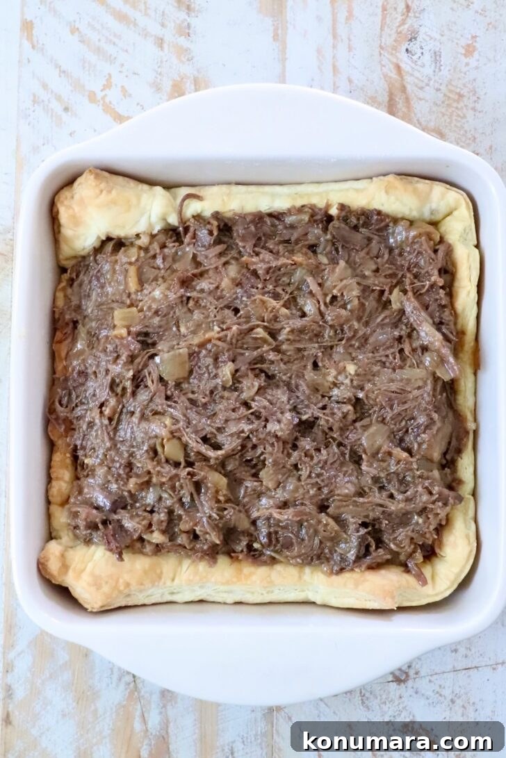 Braised Short Rib Pot Pie with French Onion 15 shredded beef filling inside of puff pastry dough in a square baking dish