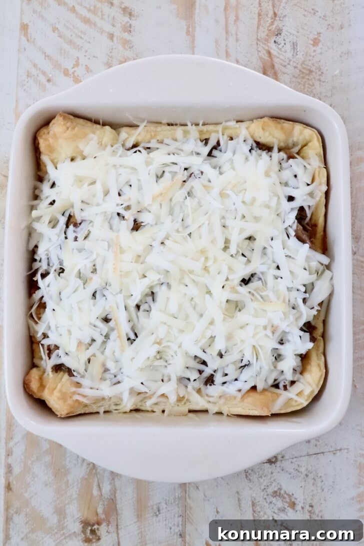 Braised Short Rib Pot Pie with French Onion 16 shredded cheese on top of shredded beef filling inside of puff pastry dough in a square baking dish
