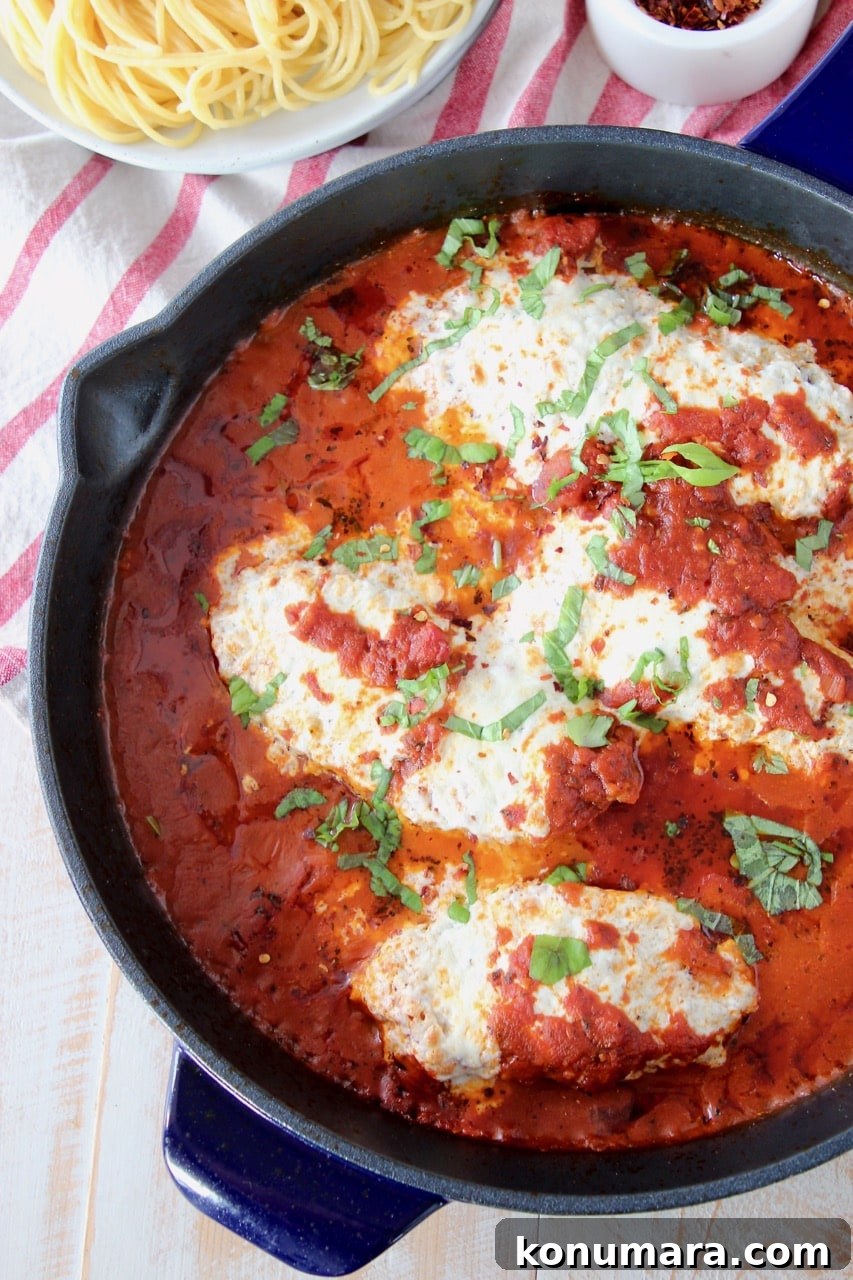 Gluten free chicken parmesan covered in marinara sauce in large cast iron skillet with a bowl of spaghetti noodles on the side