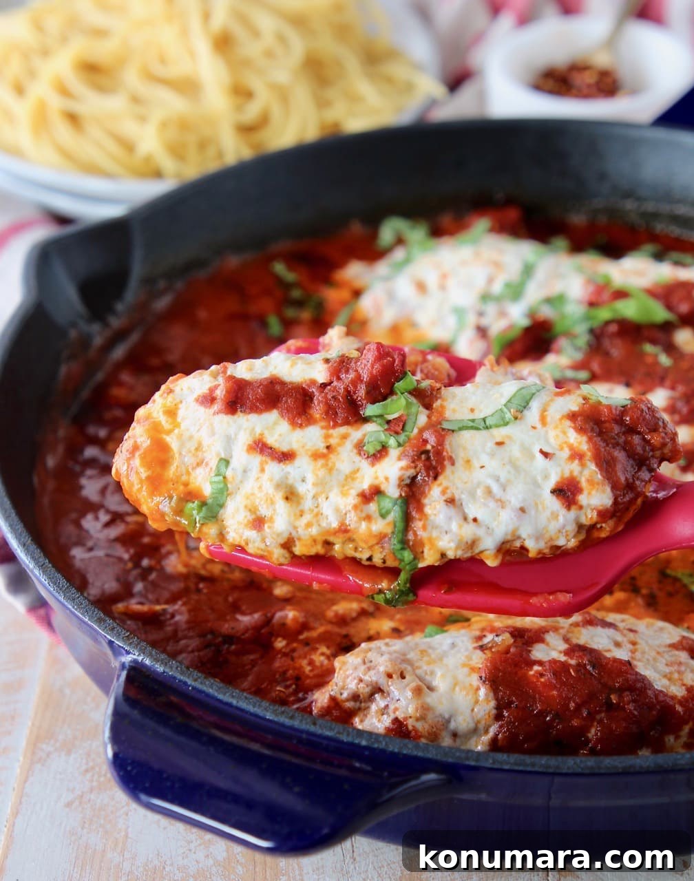 Spatula holding piece of chicken parmesan out of large skillet