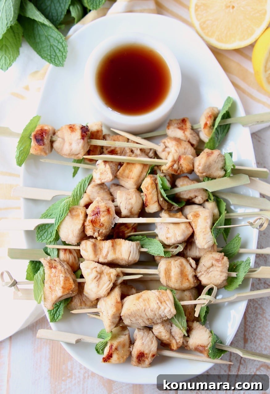 Overhead shot of chicken skewers on white plate with small bowl of bourbon sauce on the side