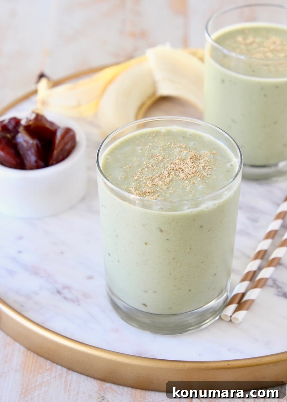 Creamy Banana and Date Protein Shake Recipe 2 Banana protein shake in two glasses sitting on white marble tray with gold and white striped straws and peeled banana in background