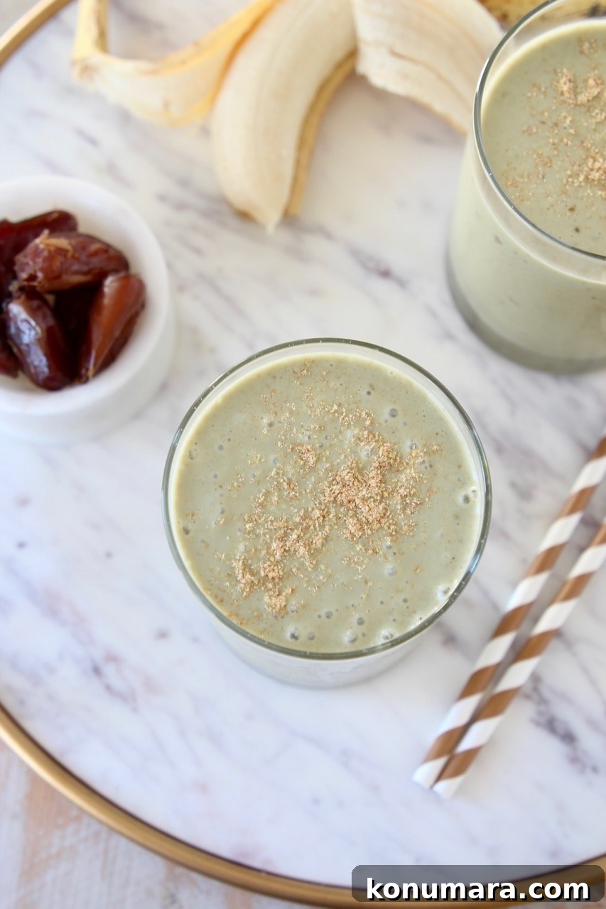 Creamy Banana and Date Protein Shake Recipe 3 Overhead shot of two banana protein shakes topped with ground flaxseed on marble tray with gold and white striped straws and a small bowl of dates on the side