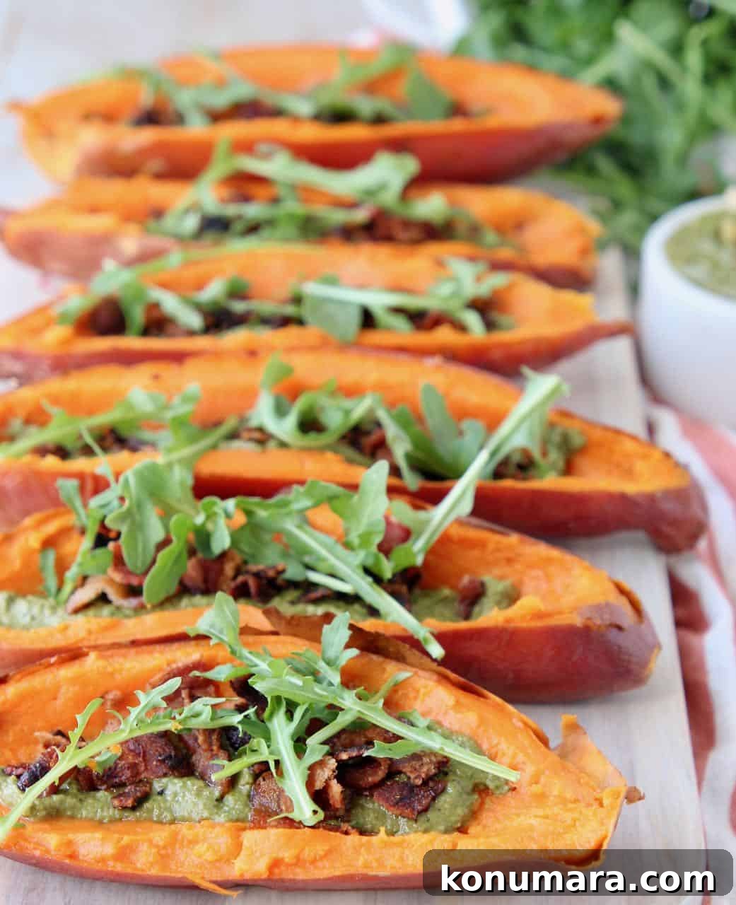 Loaded Sweet Potato Skins with Sage Pesto and Crispy Bacon 5 Sweet potato skins topped with arugula on wood cutting board
