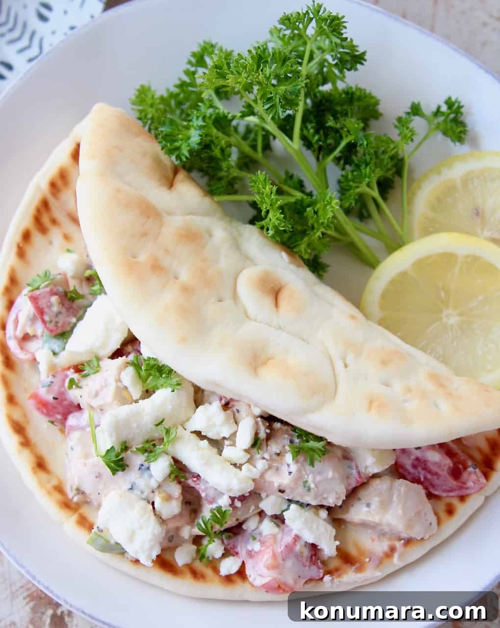 Greek Chicken Salad Pita with Tzatziki and Feta 5 overhead image of chicken salad in pita bread on plate with lemon wedges and parsley