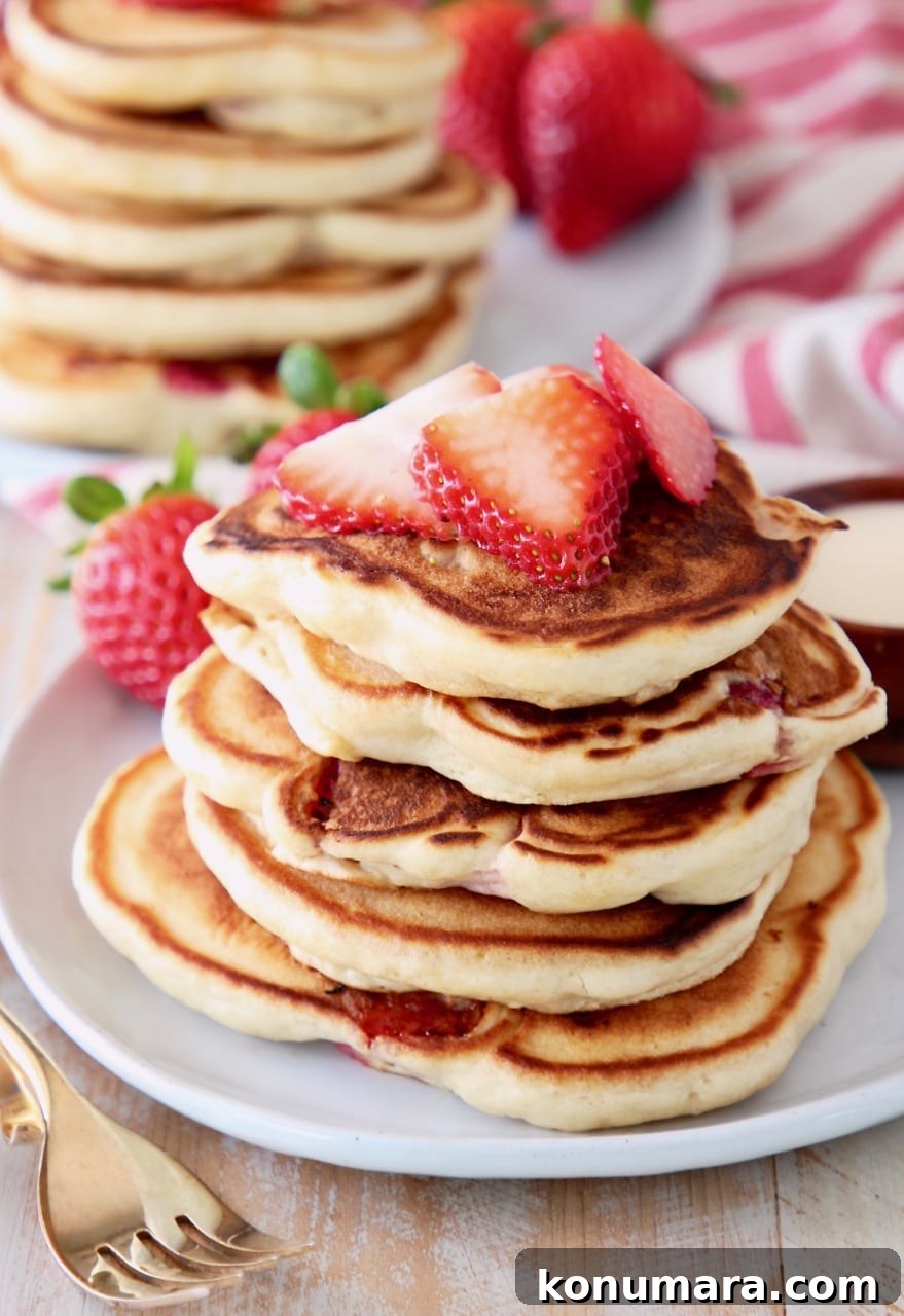 Strawberry pancakes stacked up on a plate topped with fresh strawberry slices