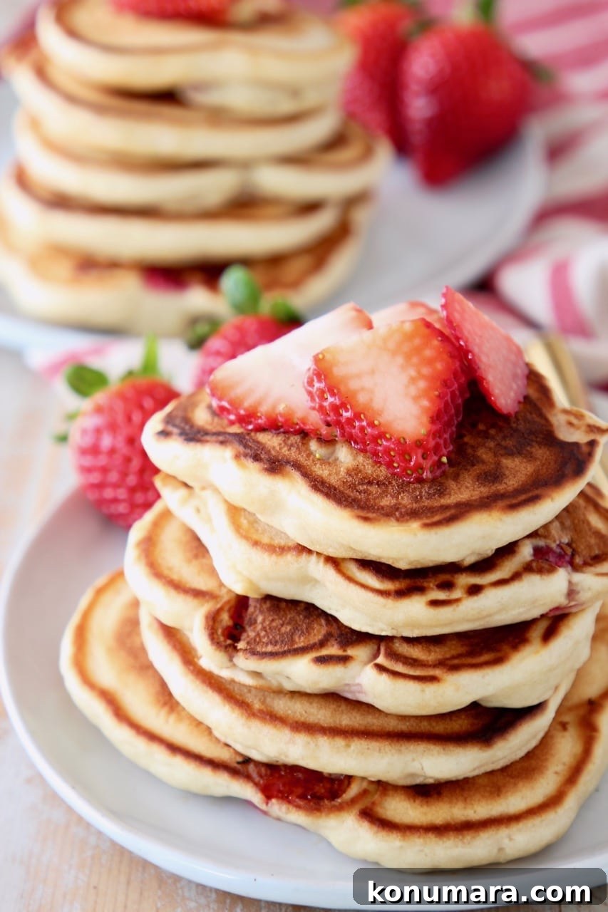 Strawberry pancakes stacked up on plate with fresh strawberries