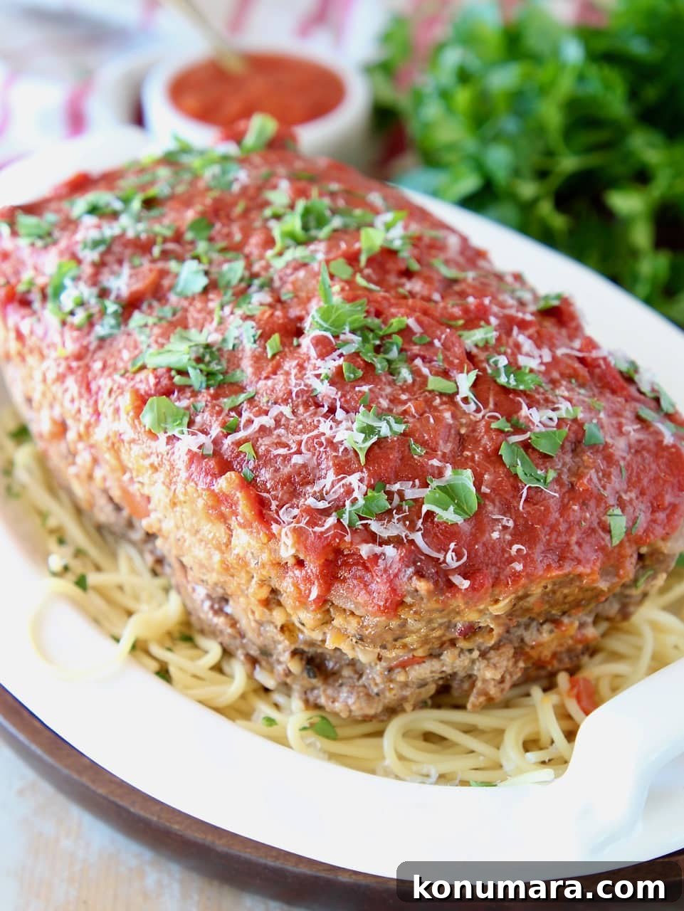 Classic Italian Meatloaf Recipe with Marinara Glaze 2 Italian meatloaf sitting on top of a bowl of spaghetti noodles, topped with fresh chopped parsley