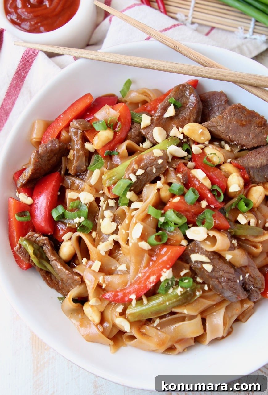 Overhead shot of Kung Pao Beef, noodles, green onions and bell peppers in bowl with chopsticks