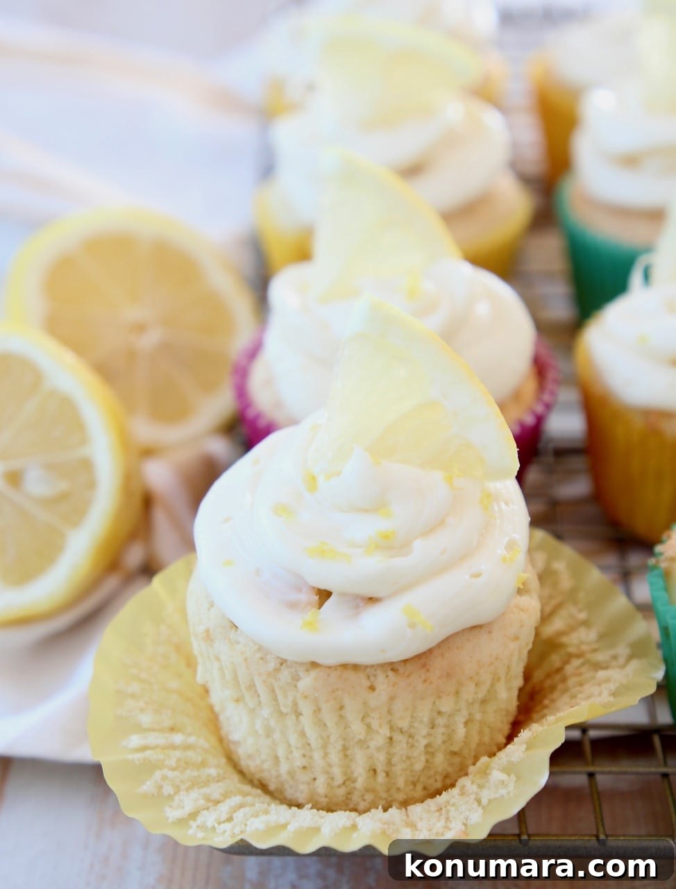 Lemon cupcake with wrapper unfolded, topped with lemon cream cheese frosting and lemon wedge