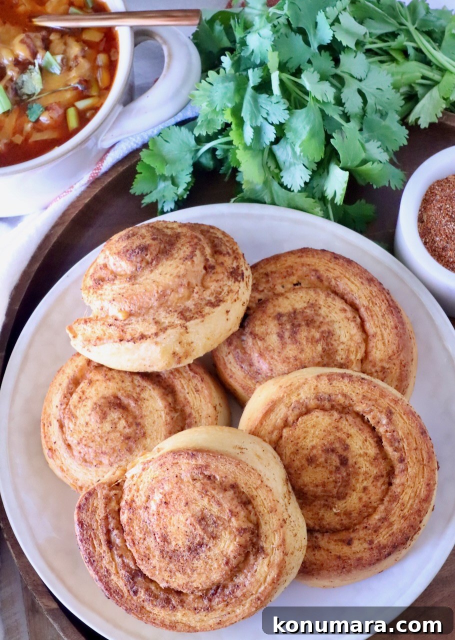 Cheesy Cornbread Rolls Recipe: Soft, Melty Centers 12 cheese-filled cornbread rolls on a plate, with a bowl of chili and fresh cilantro on the side