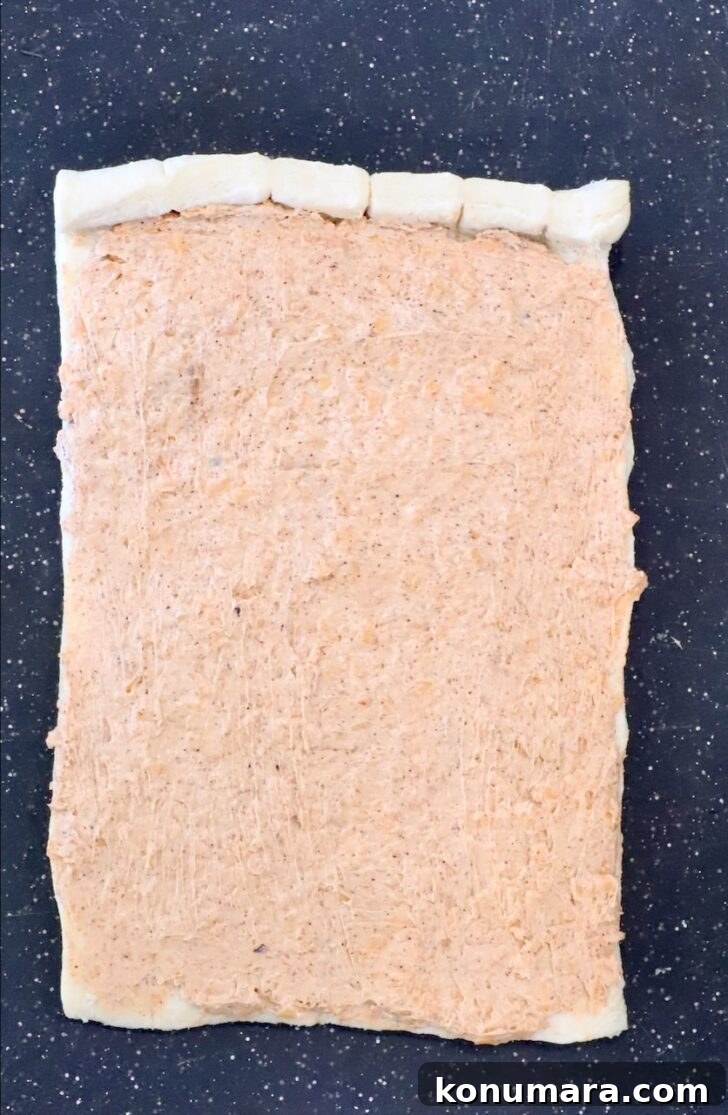 Cheesy Cornbread Rolls Recipe: Soft, Melty Centers 8 seasoned cream cheese spread on cornbread dough on a black cutting board