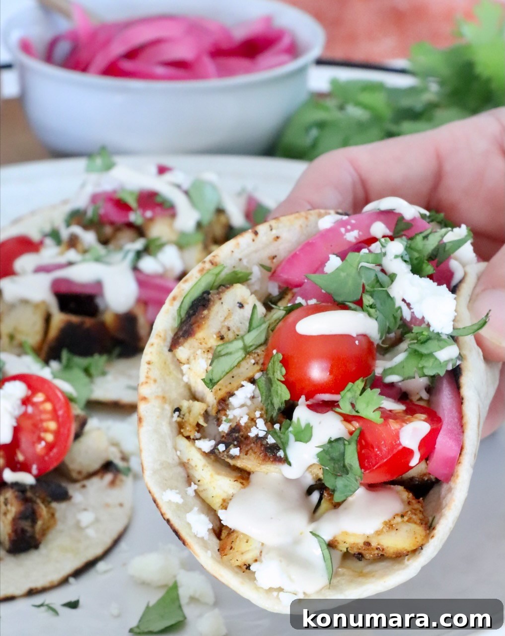 Chicken Shawarma Tacos with Garlic Yogurt Sauce 2 hand holding up a chicken shawarma taco over a plate with more tacos