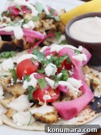 Chicken Shawarma Tacos with Garlic Yogurt Sauce 11 chicken shawarma tacos topped with pickled onions, cilantro, and tomatoes, on a plate with a small bowl of garlic sauce