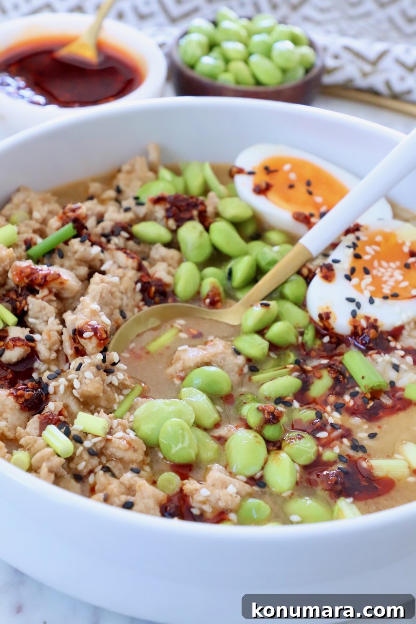 chicken broth bowl with edamame, chili crisp, and a soft-boiled egg cut in half, garnished with sesame seeds and green onions