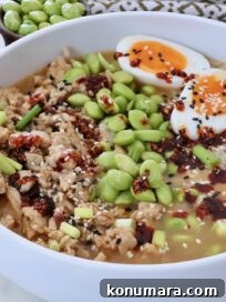bowl filled with cooked ground chicken, rice, and edamame, covered in broth, chili crisp, and sesame seeds